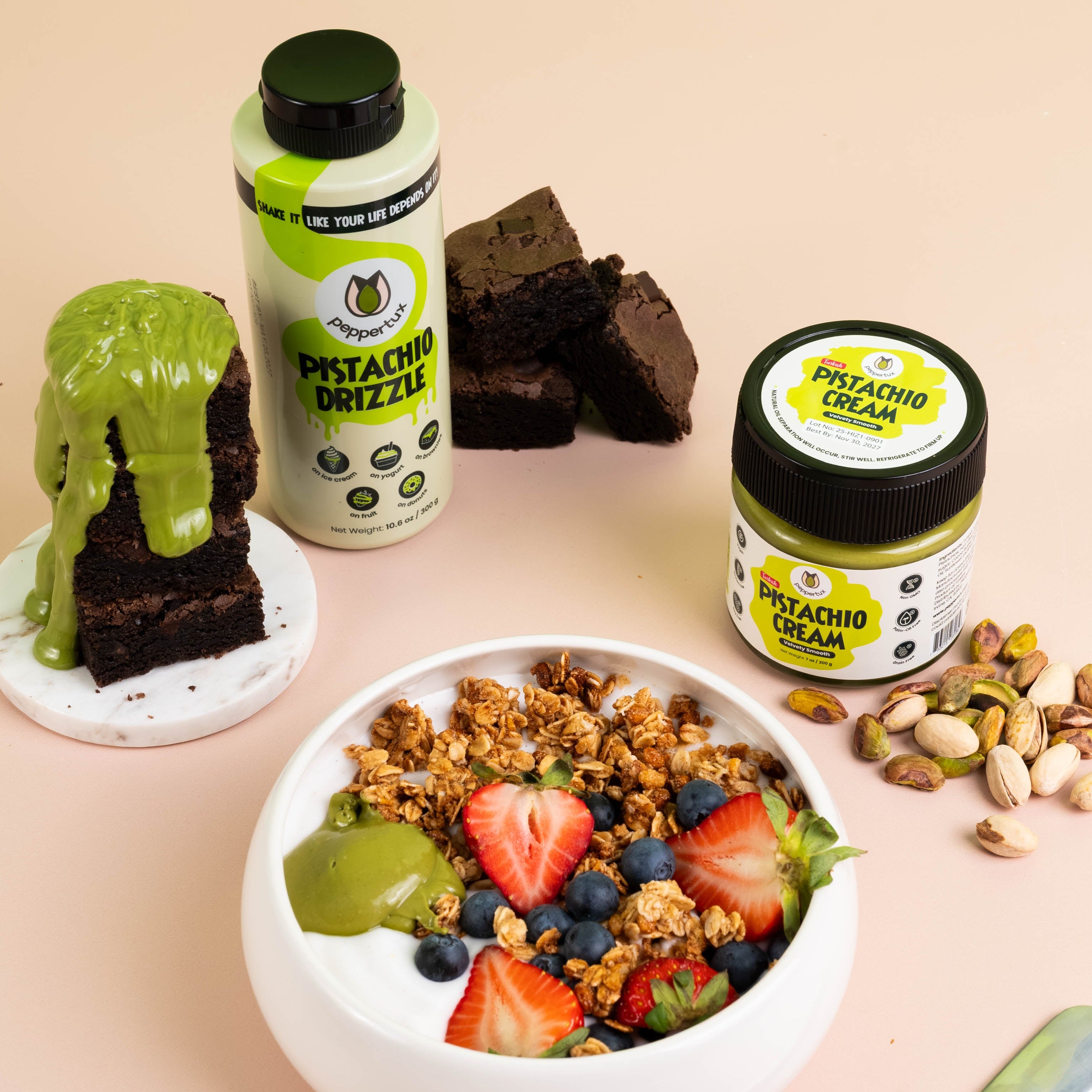 Granola bowl with fruits and Peppertux Pistachio Cream, stack of brownies with Peppertux Pistachio Drizzle on toppistachio drizzle, and cream on a beige background